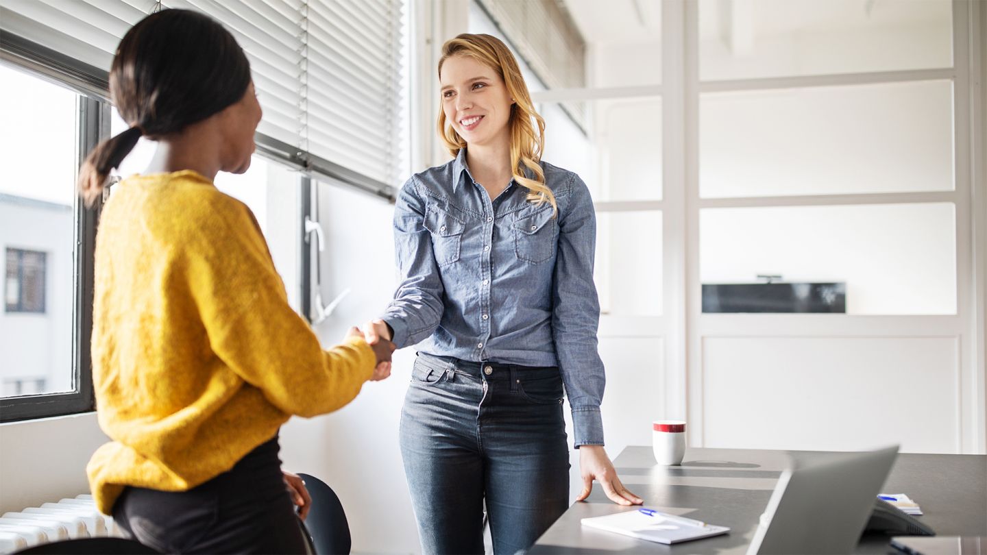 Betriebliches Eingliederungsmanagement (Quelle: Getty Images/Luis Alvarez) Betriebliches Eingliederungsmanagement: Zwei Frauen stehen an einem Bürotisch und schütteln sich nach einem erfolgreichen geschäftlichen Gespräch zustimmend die Hände.