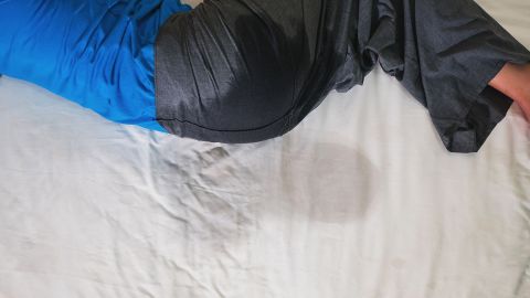 Eingenässt (Quelle: Getty Images/jes2ufoto) Enuresis: Eine erwachsene Person liegt seitlich in einem Bett. Ihre Hose weist am Gesäß eine dunkle Farbstelle auf. Auch der Bettbezug hat in Höhe des Gesäßes eine dunklere Stelle. Die Person hat sich und das Bett offenbar eingenässt.