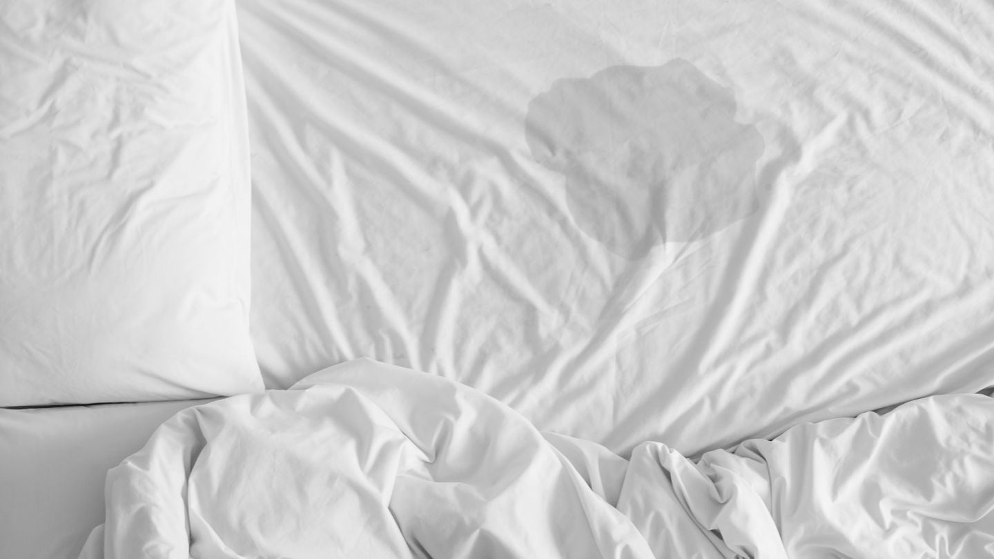 Eingenässtes Bett (Quelle: Getty Images/jes2ufoto) Bettnässen: In der Mitte eines weißen Bettbezugs, der über eine Matratze gezogen ist, ist ein größer Fleck zu sehen, der von einer Flüssigkeit stammt, offensichtlich Urin.