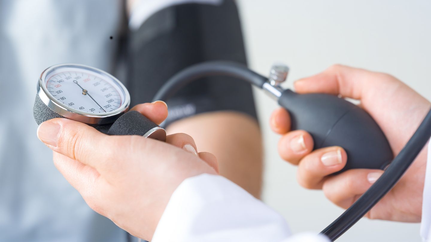 Blutdruckmessung (Quelle: iStock/Sezeryadigar) Bluthochdruck: Zwei Hände halten ein Blutdruckmessgerät. Im Hintergrund ist ein Arm zu sehen, an dem die Messmanschette befestigt ist.