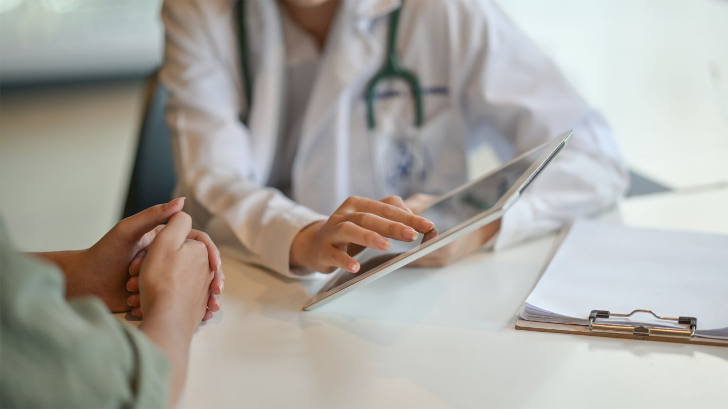 Datenschutz im Gesundheitswesen (Quelle:iStock/BongkarnThanyakij) Datenschutz: Eine Ärztin zeigt einer Patientin etwas auf einem Tablet.