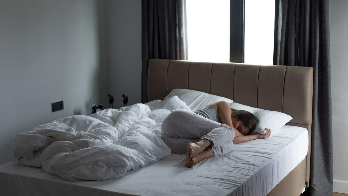 Depression (Symbolbild) (Quelle: Getty Images/bymuratdeniz) Depression: Eine Frau liegt zusammengekauert in einem großen Bett.