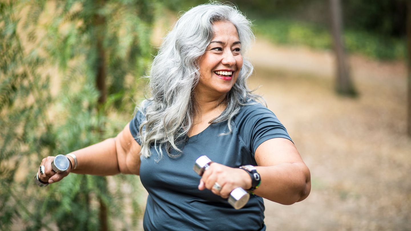 Sport bei Diabetes Typ 2 (Symbolbild) (Quelle: Getty Images/adamkaz) Diabetes Typ 2: Eine Frau hält Hanteln in beiden Händen, ist sportlich aktiv und lächelt.