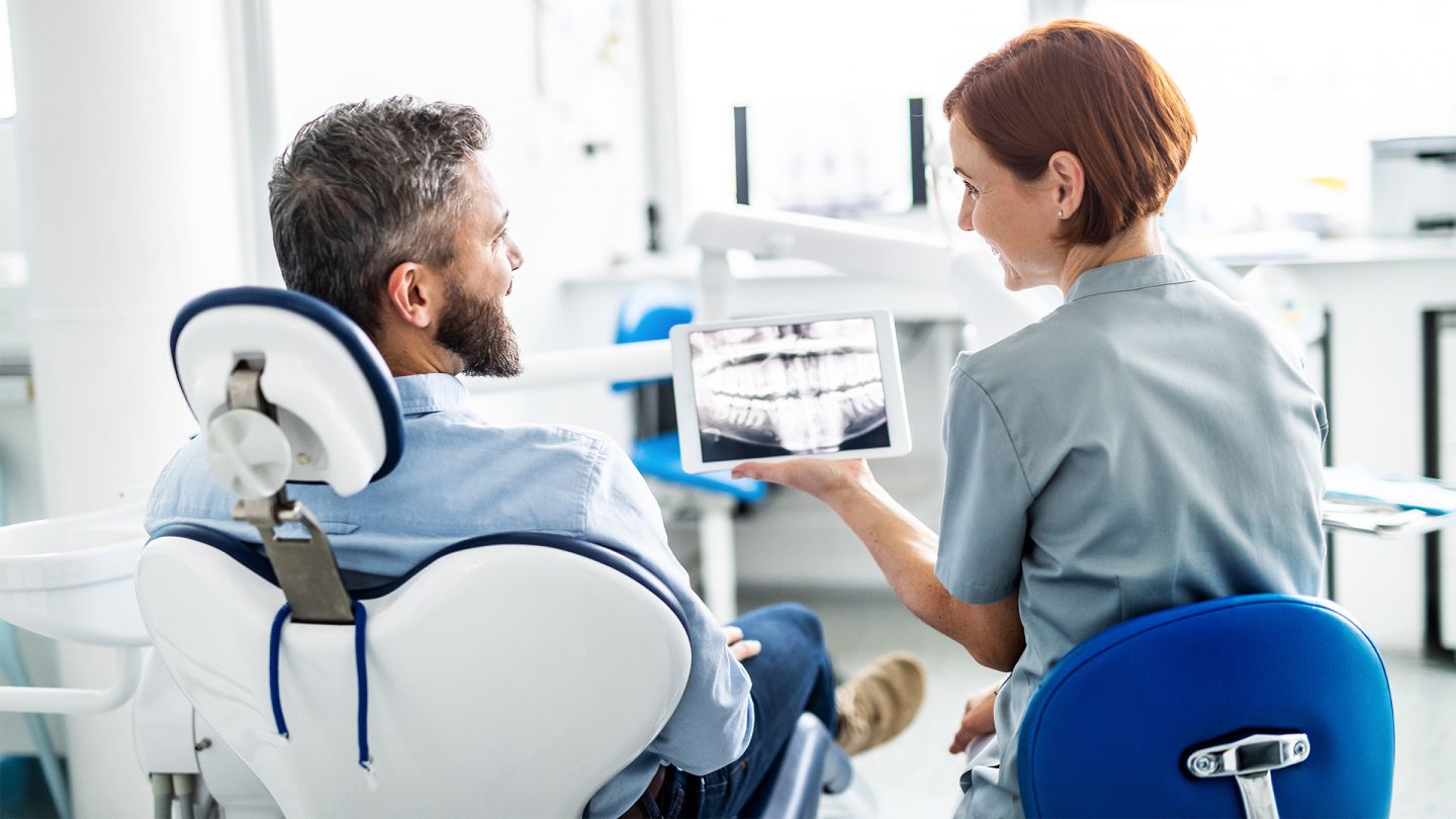 Elektronisches Zahnbonusheft (Symbolbild) (Quelle: iStock/Halfpoint) E-Zahnbonusheft: Ein Patient sitzt auf dem Behandlungstuhl beim Zahnarzt. Die Ärztin sitzt neben ihm und zeigt ihm die Röntgenaufnahme seines Gebisses auf einem Tablet.