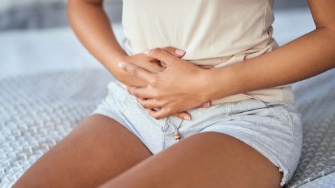 Endometriose-Symptome (Quelle: Getty Images/LaylaBird) Unterleibsschmerzen: Eine Frau sitzt auf einem Bett und hält sich mit beiden Händen den Bauch.