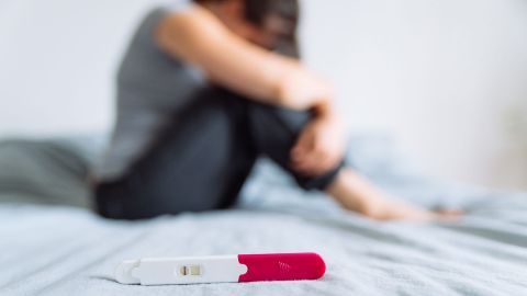 Fruchtbarkeit und Schwangerschaft (Quelle: Getty Images/Vera_Petrunina) Eine Frau kauert auf einem Bett, im Bildvordergrund, ebenfalls auf dem Bett, liegt ein negativer Schwangerschaftstest.