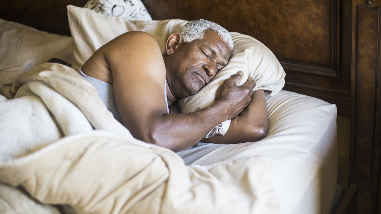 Gesunder Schlaf im Alter (Getty Images/adamkaz) Gesunder Schlaf im Alter: Ein älterer Mann liegt auf der Seite im Bett und schläft. Mit gebeugtem Arm klemmt er sich sein Kissen zwischen Kopf und Arm.