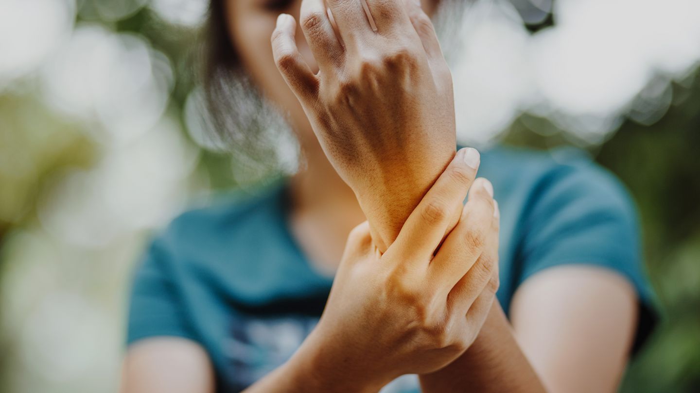 Schmerzen am Handgelenk (Quelle: Getty Images/Anut21ng) Karpaltunnelsyndrom: Eine Frau hält ihre Arme in die Luft und fasst sich ans linke Handgelenk.