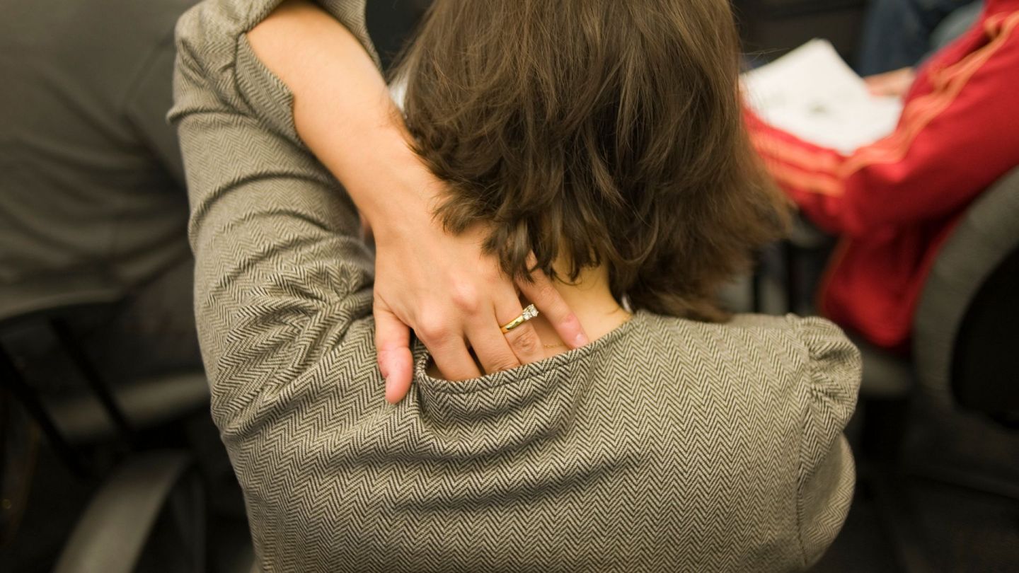 Juckende Haut (Quelle: Getty Images/Helen King) Kleienpilzflechte: Eine Frau steht mit dem Rücken zugewandt in einer Menschenmenge und greift sich mit der linken Hand an ihren Nacken.