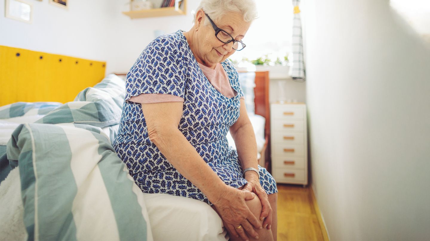 Kniearthrose (Quelle: Getty Images/Eva-Katalin) Eine ältere Dame sitzt auf dem Bett und fasst sich an das schmerzende Knie.
