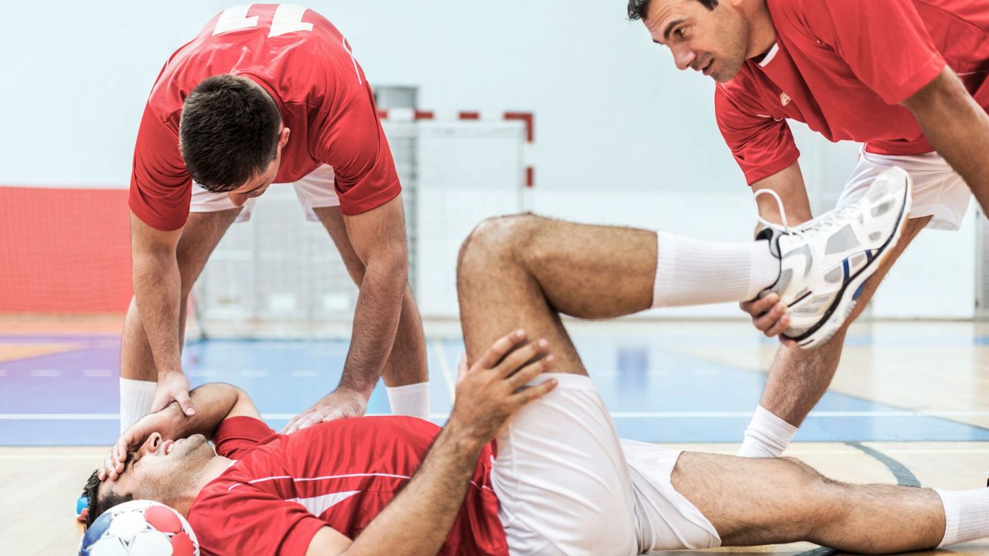 Verletzter Fußballer (Symbolbild) (Quelle: Getty Images/skynesher) Kreuzbandriss: Ein Fußballer liegt mit schmerzverzerrtem Gesicht auf dem Boden, fasst sich mit einer Hand an den Kopf und mit der anderen Hand an sein Bein. Ein Mitspieler steht daneben und stützt den Fuß des Verletzten.