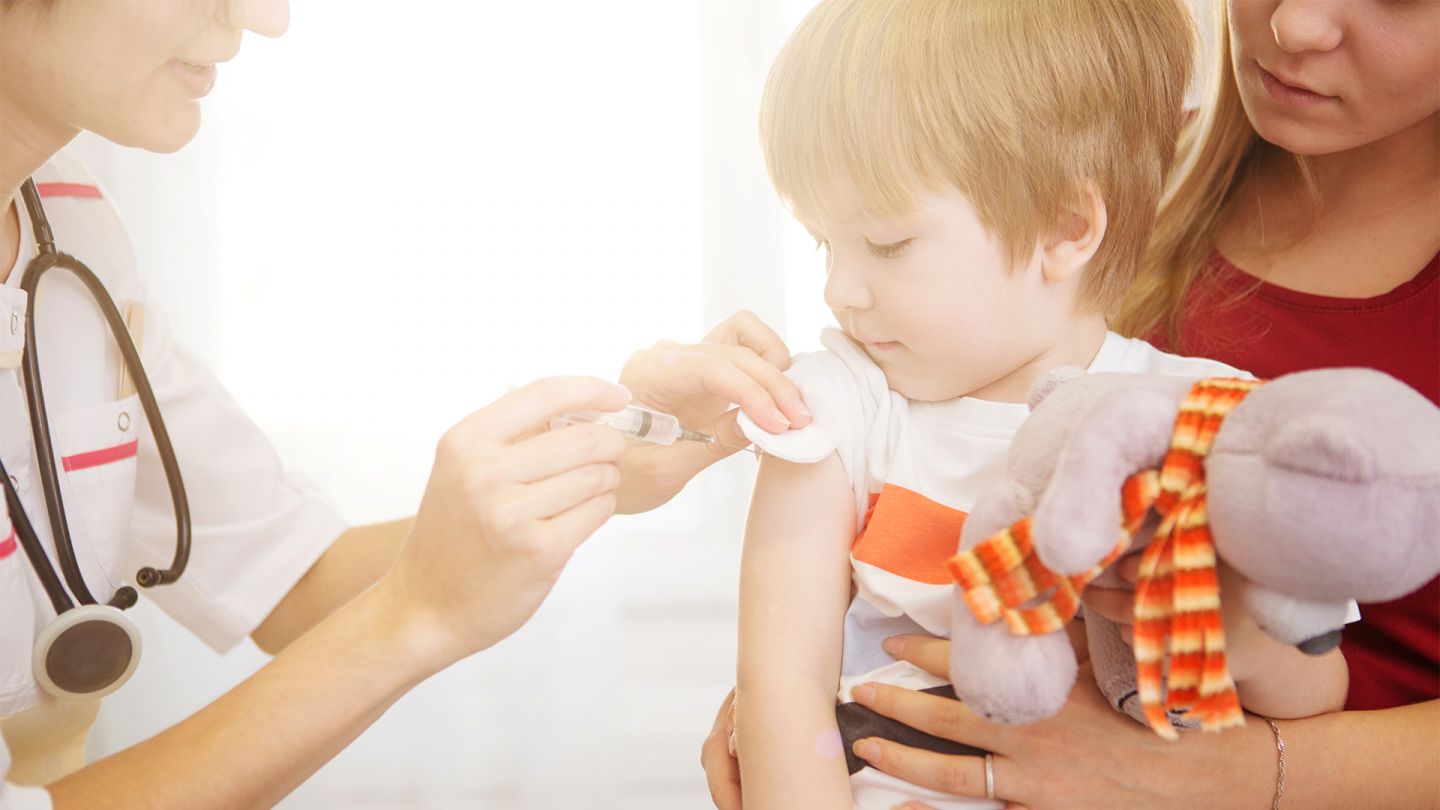 Masern (Quelle: Getty Images/AlekZotoff) Masern: Ein Kind sitzt auf dem Schoß der Mutter und bekommt von einer Kinderärztin eine Impfung in den Oberarm.