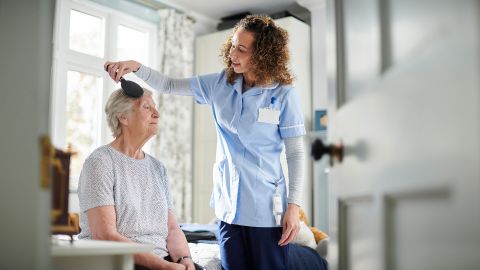 Haarpflege (Quelle: Getty Images/sturti) Eine ältere Frau sitzt am Bettrand. Neben ihr steht eine junge Frau. Sie kämmt der älteren, offenbar pflegebedürftigen Frau die Haare.