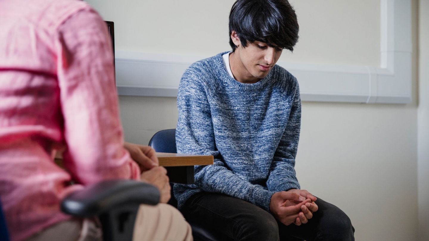 Jugendlicher mit Phimose (Symbolbild) (Quelle: Getty Images/SolStock) Phimose: Ein Jugendlicher sitzt auf einem Stuhl in einem Behandlungszimmer. Seine Hände liegen in seinem Schoß, er wirkt bedrückt.