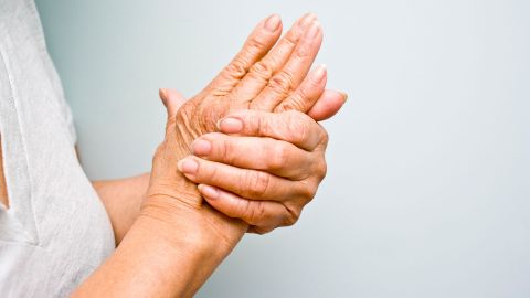 Schmerzen an der Hand (Quelle:Getty Images/michellegibson) Rheuma: Eine stehende Frau hält beide Arme vor die Brust. Mit einer Hand greift die Frau an das Gelenk der anderen Hand.