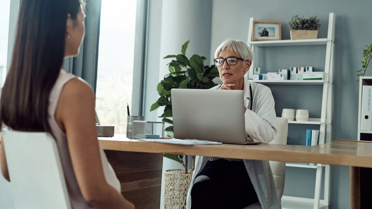 Ärztin und Patientin (Symbolbild) (Quelle: Getty Images/Dean Mitchell) Scheidenpilz: Eine Frau sitzt in einem Behandlungszimmer. Ihr gegenüber sitzt eine Ärztin und guckt auf ihren Laptop.