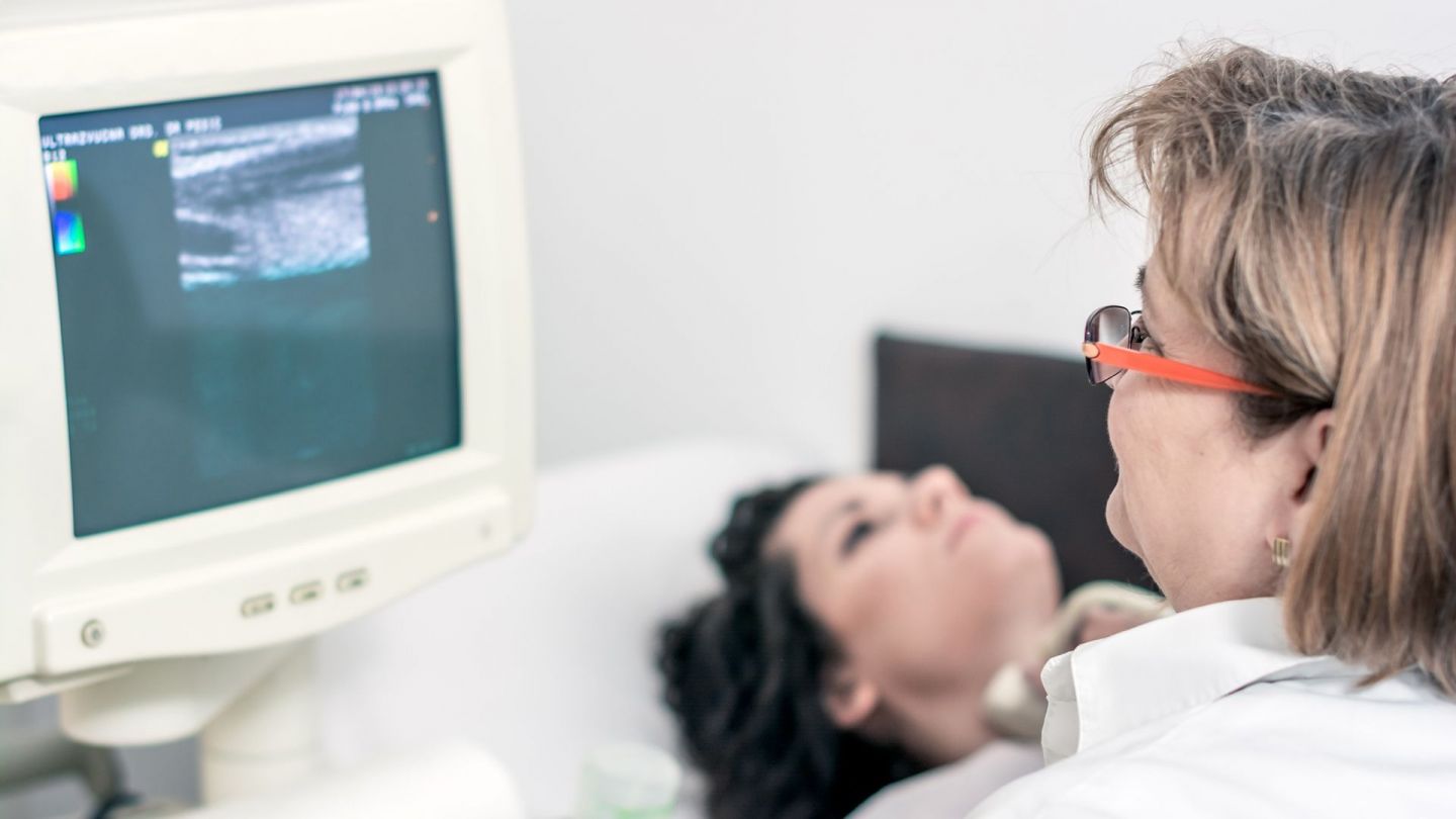 Ultraschalluntersuchung der Schilddrüse (Symbolbild) (Quelle: Getty Images/Marizza) Schilddrüsenkrebs: Eine Patientin liegt auf einer Krankenhausliege. Vor ihr sitzt eine Ärztin und führt eine Ultraschalluntersuchung ihrer Schilddrüse durch. Die Ärztin beobachtet das Ultraschallbild auf einem Monitor.