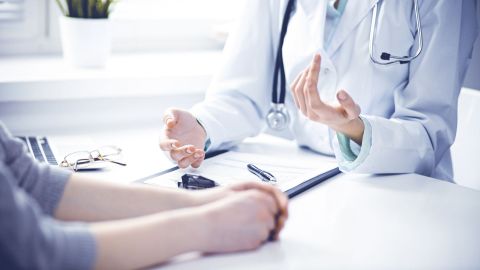 Sprechstunde in der Praxis (Quelle: Getty Images/andrei_r) Eine Ärztin und eine Patientin sitzen an einem Tisch. Sprechen miteinander. Die Patientin holt sich eine Zweitmeinung ein. Vor der Ärztin auf dem Tisch liegt ein ausgedrucktes Dokument aus einer Patientenakte.