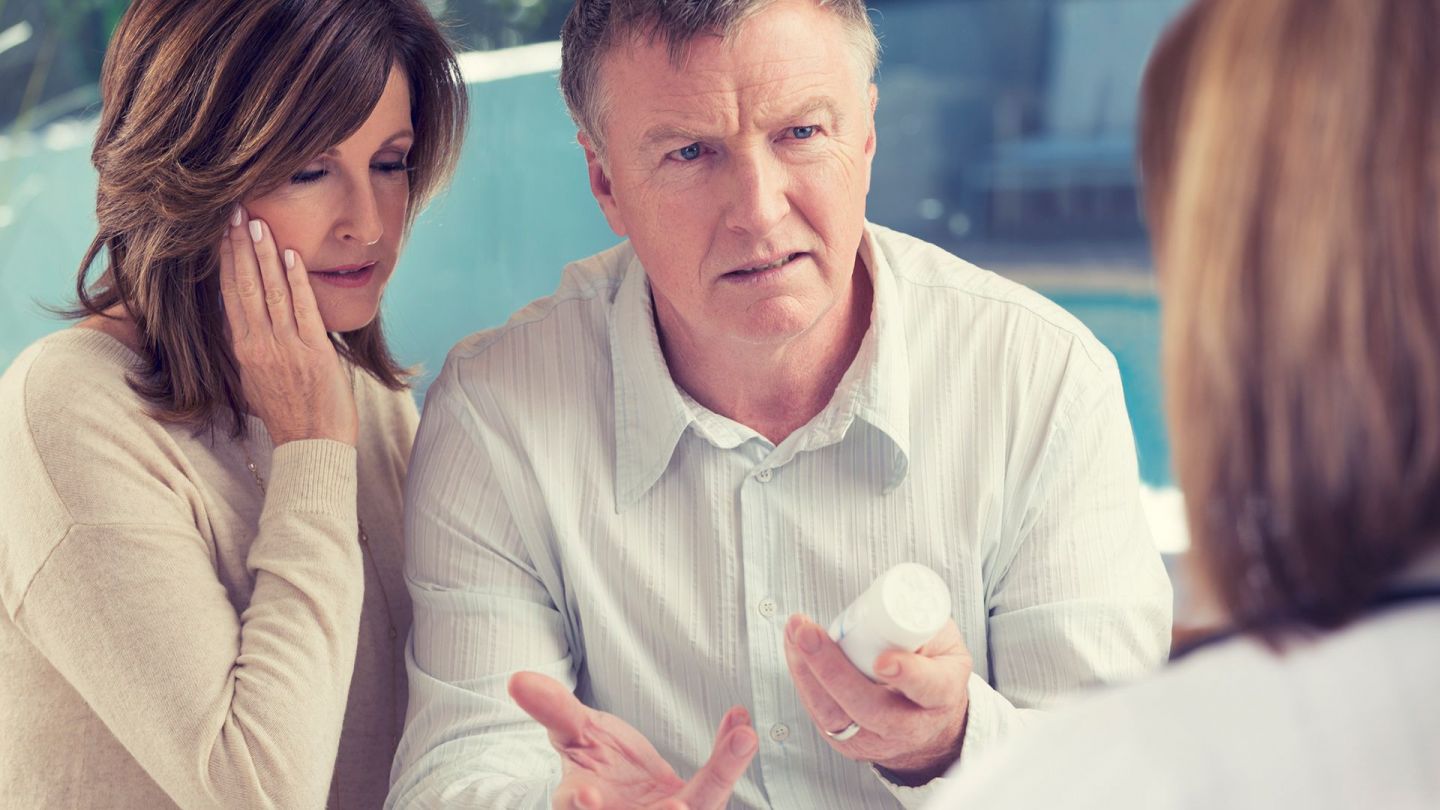 Gespräch mit Ärztin (Symbolbild) (Quelle: Getty Images/courtneyk) Beschwerde über ärztliche Behandlung: Ein Mann und eine Frau stehen dicht beinander, eine Ärztin steht ihnen gegenüber. In einer Hand hält der Mann ein Medikament. Er schaut die Ärztin fragend an.
