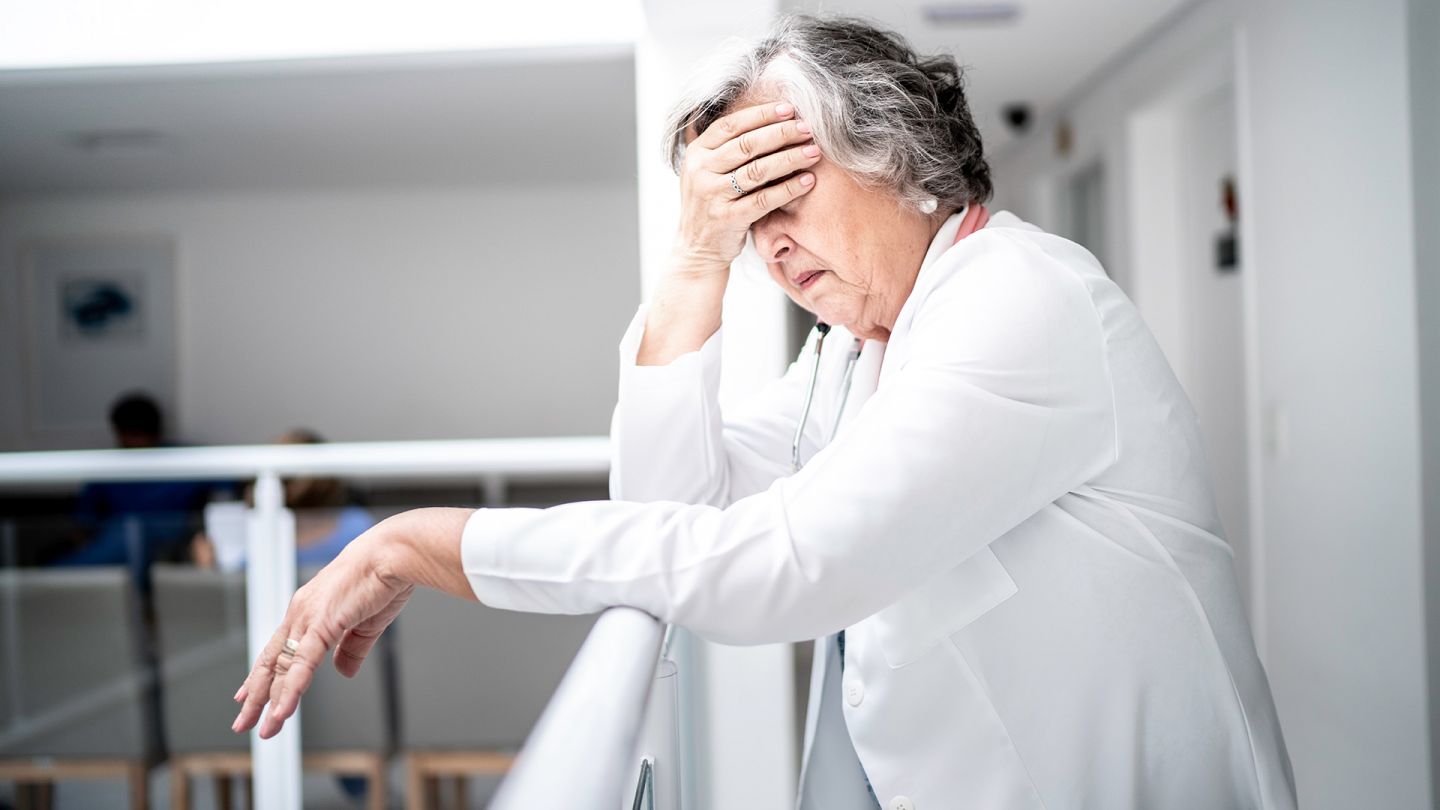 Kopfschmerzen (Quelle: Getty Images/FG Trade) Spannungskopfschmerzen: Eine ältere Frau lehnt an einem Geländer und fasst sich mit einer Hand an die Stirn. Die Frau wirkt erschöpft.