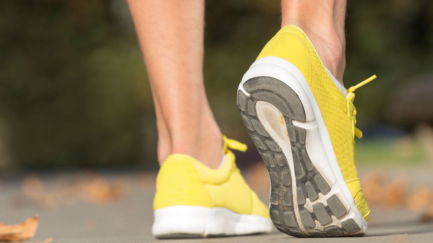 Jogger (Quelle: Getty Iamges/m-gucci) Sprunggelenkverstauchung: Ein Jogger steht mit beiden Beinen auf einer asphaltierten Lauffläche. Das rechte Bein zieht der Sportler an der Ferse etwas nach oben an, sodass er bei einem Bein nur auf dem Fußballen steht.