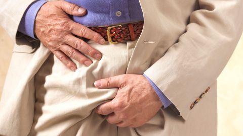 Schmerzen an den Hoden (Quelle: Getty Images/Peter Dazeley) Krampfadern am Hoden: Ein älterer Mann steht auf einer Treppe. Mit der linken Hand packt sich der Mann an den Schritt. Mit der anderen Hand greift er sich ans Becken.