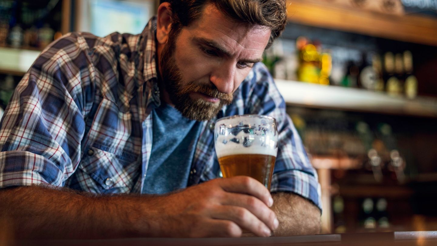 Biertrinker (Quelle: Getty Images/PhotoAlto/Frederic Cirou) Alkohol: Ein Mann sitzt alleine in einer Bar, lehnt sich mit beiden Armen auf den hölzernen Tresen, hält ein Bierglas in der Hand und schaut in den Glas.
