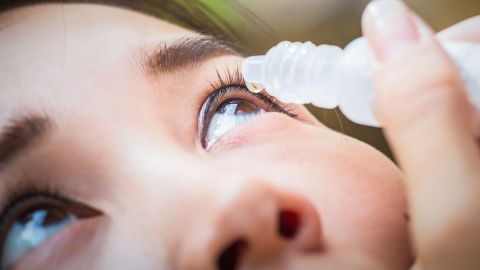 Augentropfen (Quelle: Getty Images/Jay_Zynism) Entzündete Bindehaut: Eine junge Frau verabreicht sich Augentropfen. Sie hat ihren Kopf in den Nacken gelegt und schaut in den Himmel. Mit einer Hand hält die Frau eine kleine Plastikflasche über ein Auge. Aus der Flaschenöffnung läuft ein Tropfen.