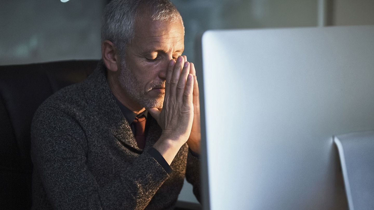 Burn-out (Symbolbild) (Quelle: Getty Images/Peopleimages) Burn-out: Ein Mann sitzt mit geschlossenen Augen vor einem Bildschirm und fasst sich an die Stirn.