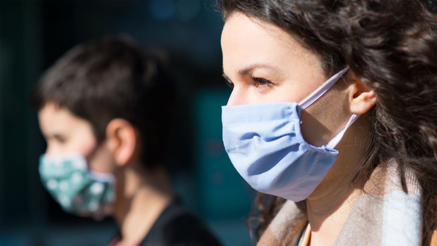 Mund-Nase-Schutz in öffentlichen Verkehrsmitteln (Quelle: iStock.com/HbrH) Eine junge Frau steht in einem Bus. Sie trägt einen Mund-Nase-Schutz und hält sich die Hand ans Gesicht. Sie wirkt erschöpft.
