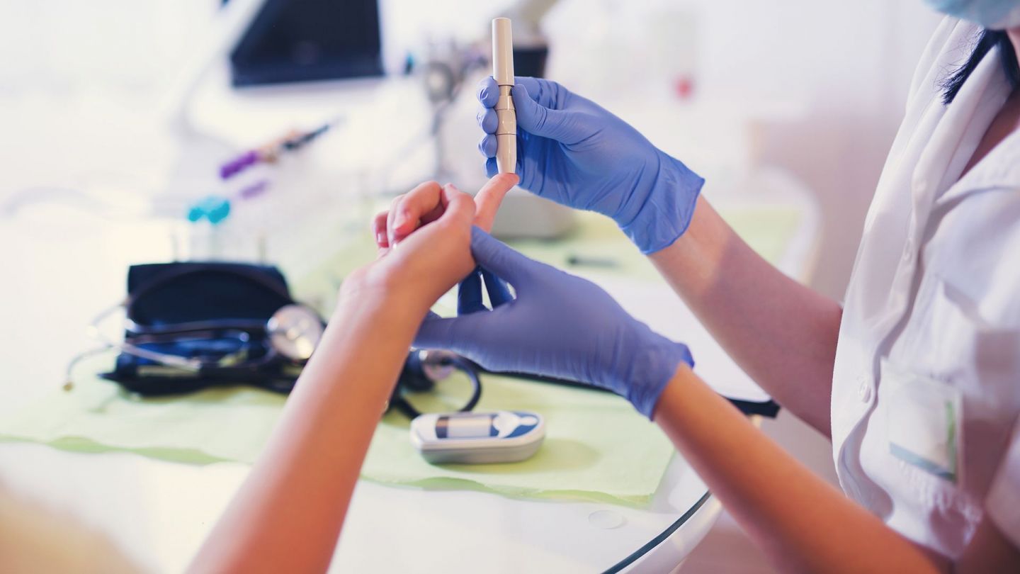 Diabetes-Typ-1-Blutzuckermessung (Quelle: Getty Images/Jovanmandic) Diabetes Typ 1: Eine Ärztin hält ein Blutzuckertestgerät an die Fingerkuppe einer Frau..