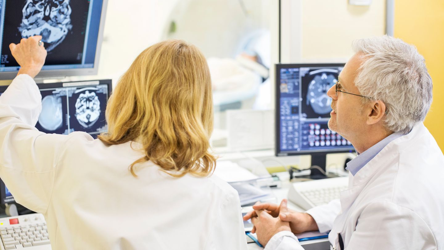 Epilepsie-Untersuchung (Quelle: Getty Images/alvarez) Epilepsie: Eine Ärztin und ein Arzt begutachten das gescannte Bild eines Schädels und Gehirns auf einem Monitor.