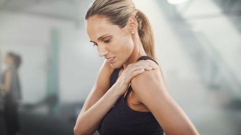Funktionelle Koerperbeschwerden Symptome (Quelle: Getty Images / Jay Yuno) Eine Frau in Sportkleidung und leicht schmerzverzerrtem Blick greift sich an die Schulter.