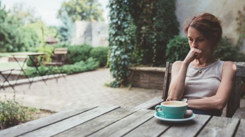 Sorgen im Alltag (Symbolbild) (Quelle: Getty Images/martin-dm) Eine Frau sitzt an einem Tisch in einem Garten, stütz ihren Kopf auf ihrer Hand ab und blickt auf den Tisch. Die Frau scheint besorgt zu sein.