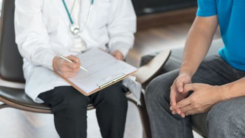 Arzt befragt Patient (Quelle: Getty Images/Pornpak Khunatorn) Ein Urologe hält einen Fragebogen und einen Stift in der Hand, neben ihm sitzt ein Mann.
