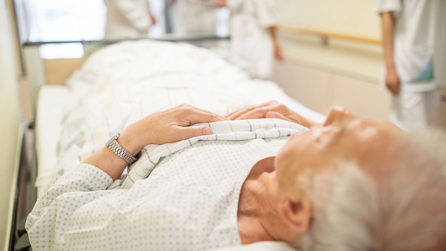 Im Krankenhaus (Quelle: getty Images/alvarez) Harnblasenkrebs: Ein älterer Mann liegt mit dem Rücken auf einem Behandlungsbett, das durch den Gang eines Krankenhauses geschoben wird. Um den Mann herum stehen vier Menschen, die weiße Kittel tragen.