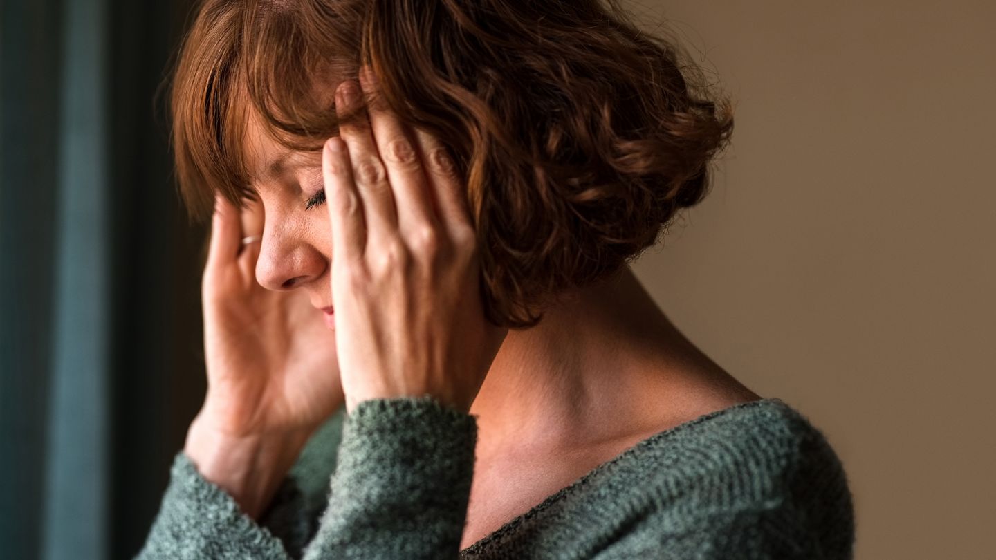 Migräne (Symbolbild) (Quelle: Getty Images/NickyLloyd) Migräne: Eine Frau fasst sich mit beiden Händen an den Kopf.