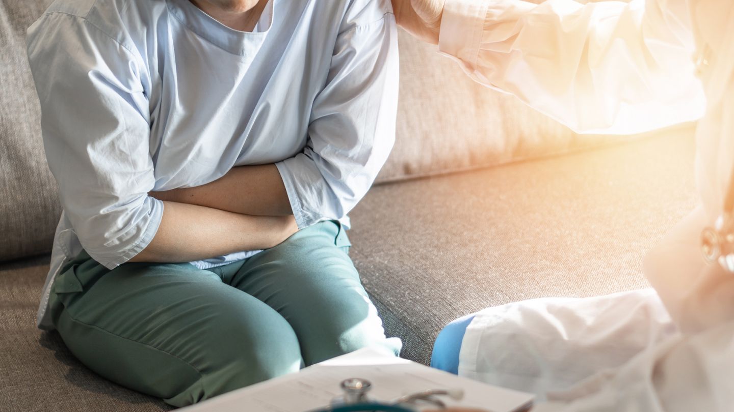 Bauchschmerzen (Quelle: Getty Images/Chinnapong) Reizdarmsyndrom: Eine Frau sitzt auf einer Couch, hält ihre Arme verschlossen und presst sie an ihren Bauch. Die Frau hat ihren Oberkörper leicht nach vorne gebeugt und presst auch ihre Oberschenkel zusammen. Die Körperhaltung wirkt angespannt.