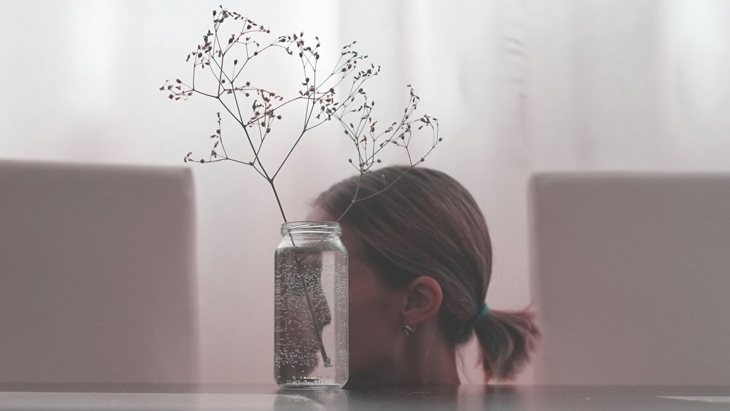Junge Frau mit Schizophrenie (Symbolbild) (Quelle: Getty Images/Tatyana Maximova) Schizophrenie: Abgebildet ist das Profil einer jungen Frau. Ihr Gesicht ist hinter einer durchsichtigen Blumenvase verborgen. Das Gesicht der Frau spiegelt sich verkehrt herum im Glas.