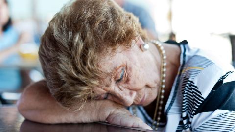 Atemaussetzer im Schlaf (Symbolbild) (Quelle: Getty Images/Juanmonino) Eine ältere Frau stützt ihren Kopf auf ihren Arm, der auf einem Tisch liegt. Sie scheint zu schlafen.