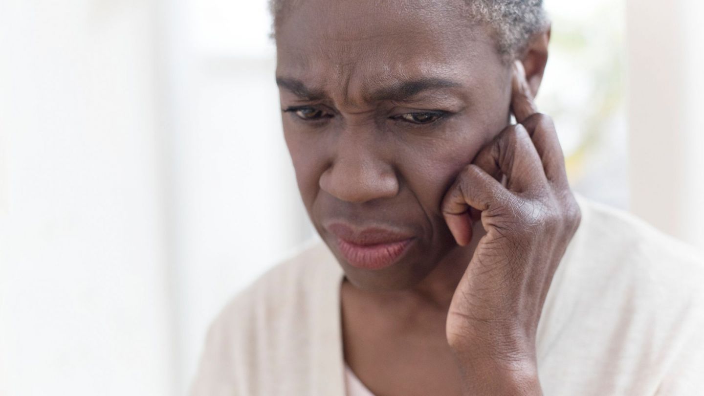 Tinnitus (Quelle: Getty Images/Science Photo Library) Tinnitus: Eine Frau fasst sich mit einem Finger ans Ohr und schaut skeptisch.