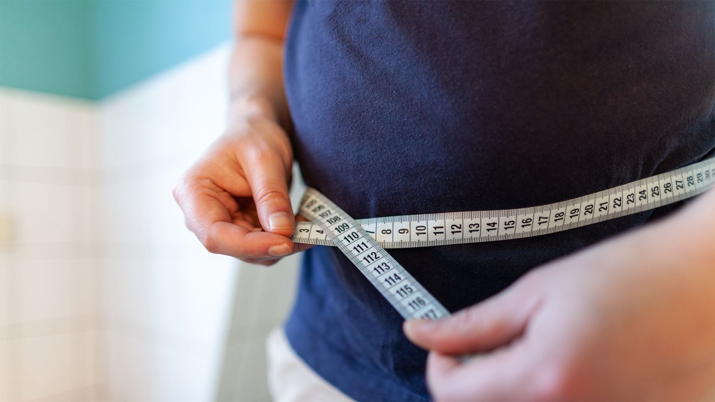 Übergewicht (Quelle: Getty Images/huettenhoelscher) Übergewicht: Ein Mann misst seinen Bauchumfang mit einem Maßband, das er mit beiden Händen vor dem Bauch zusammenhält.